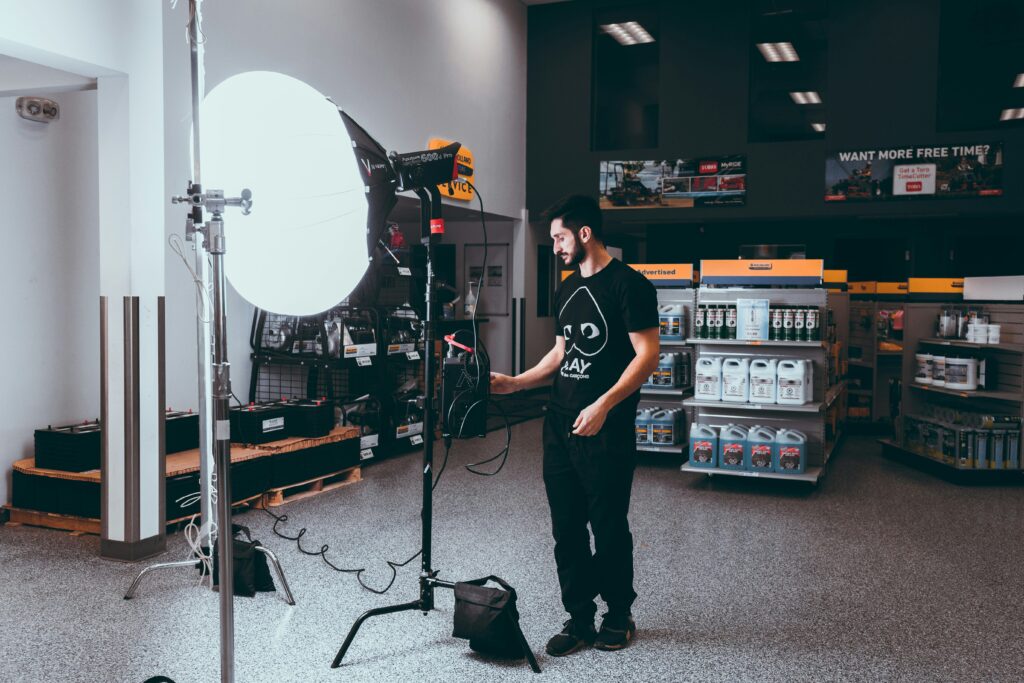 alt="Adult man in a photoshoot holding a camera bag beside an equipment case"