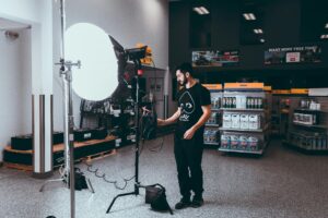 alt="Adult man in a photoshoot holding a camera bag beside an equipment case"