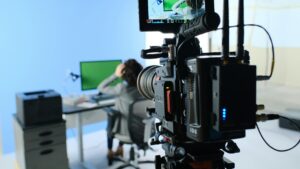 alt="A camera recording a person in front of a screen"