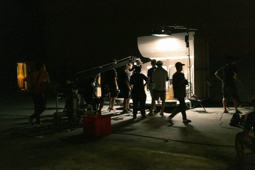 a group of people standing around a camera in a video production set the dark